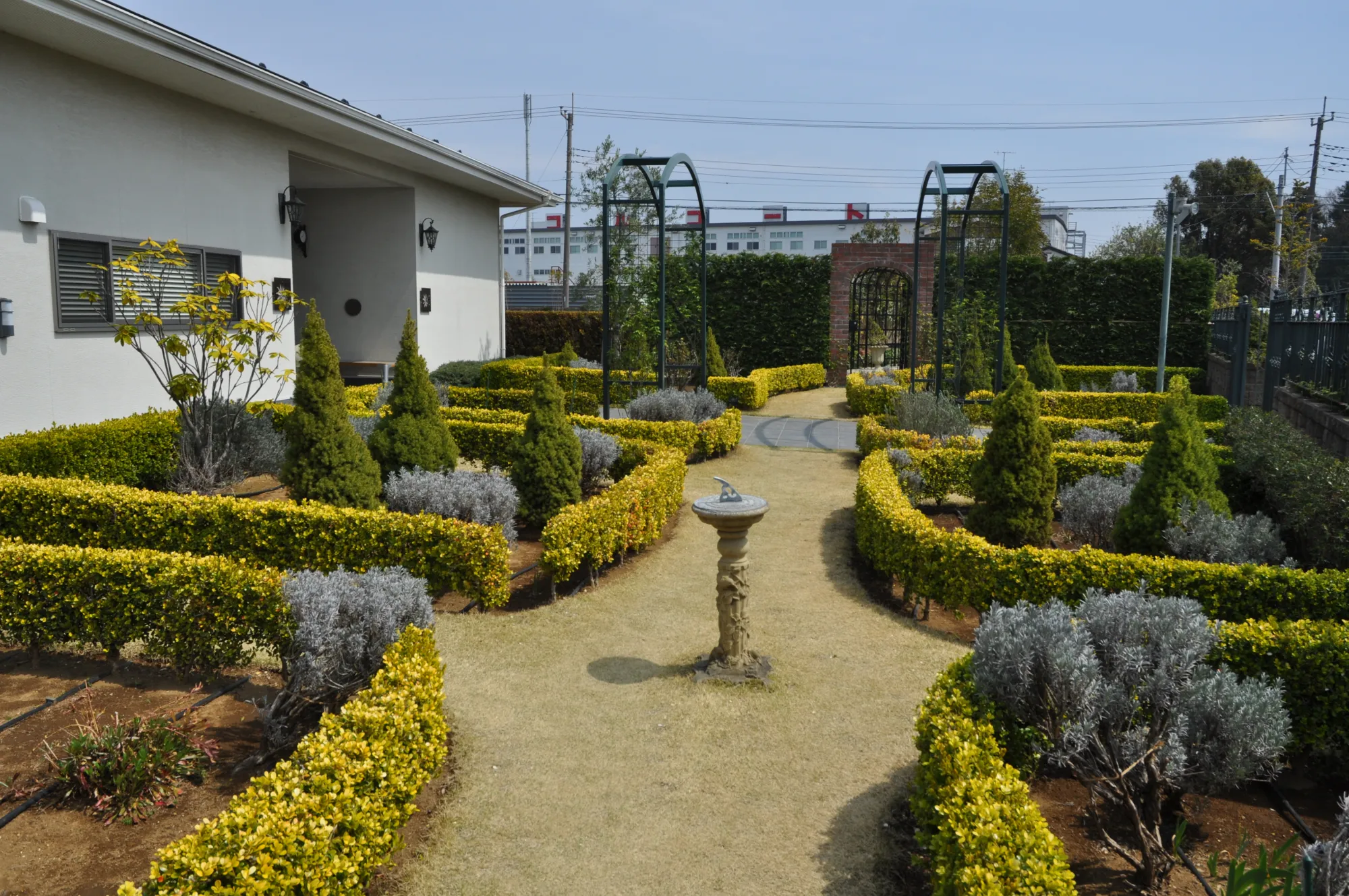 砂利の小径と日時計、奥にレンガ門がある庭園